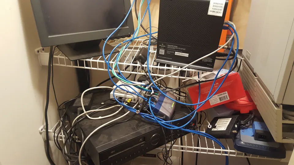 A closet crowded with network and video equipment and tangled cables