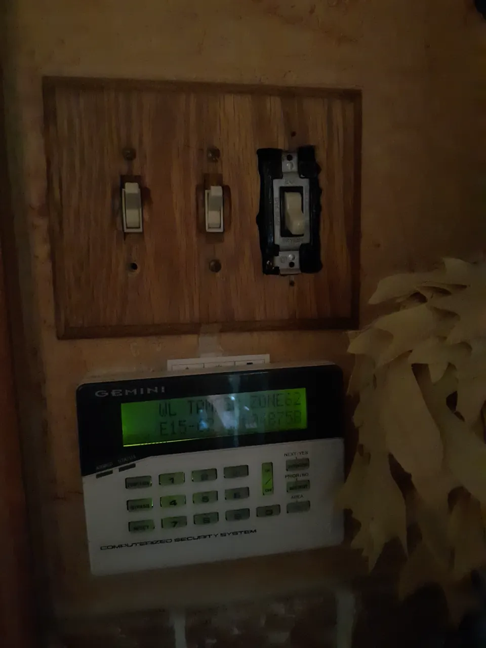 An alarm keypad mounted beneath mismatched and damaged electrical switches
